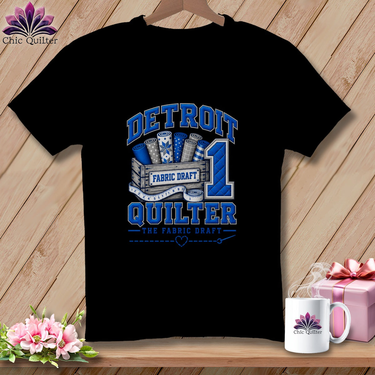 A black t-shirt features a blue graphic with a crate of fabric rolls, a number one, and the text Detroit Quilter.