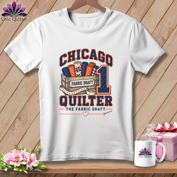 A white t-shirt features a graphic with Chicago Quilter text, fabric bolts in a crate, and a measuring tape.