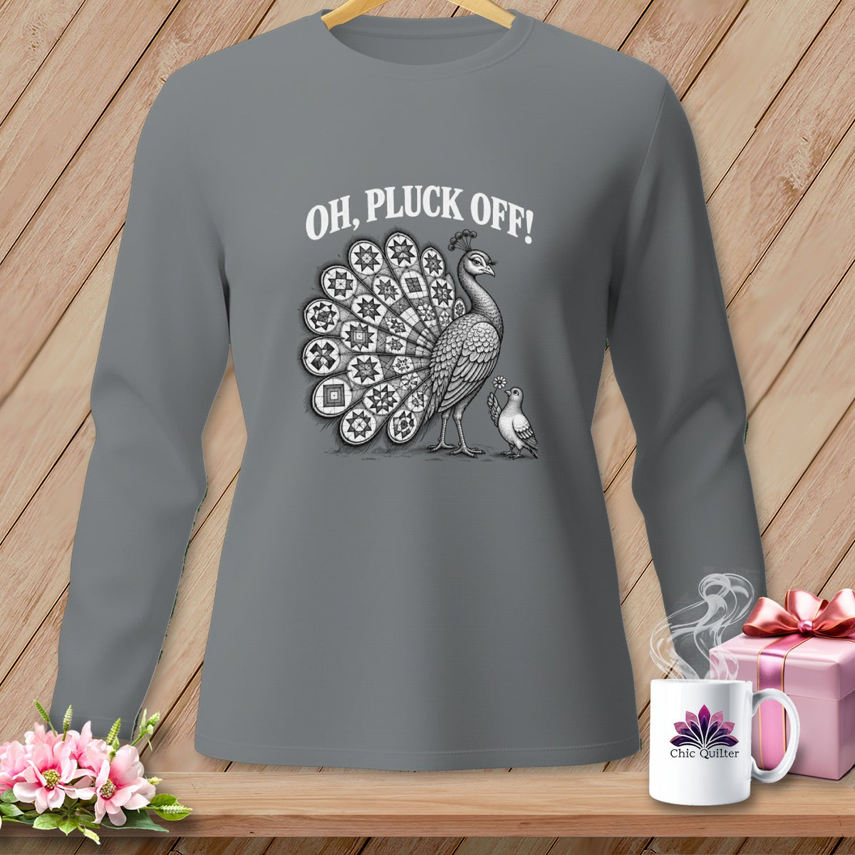 A dark gray long-sleeved shirt features a graphic of a peacock with quilt-patterned feathers and the text OH, PLUCK OFF!