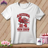 A white t-shirt hanging on a wooden wall displays a red cardinal graphic, the text Arizona 24 Sew Crew, and spools of thread.
