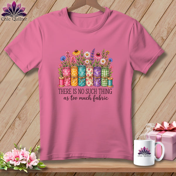 Pink short-sleeve t-shirt featuring rolled fabric graphic with flowers and text, hanging against wood background.