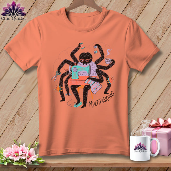 Spider sewing with coffee, scissors, and "Multitasking" text on a peach t-shirt.
