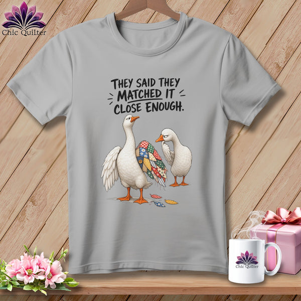 Gray t-shirt with two geese, one with a patchwork wing, and text "They said they matched it - close enough."