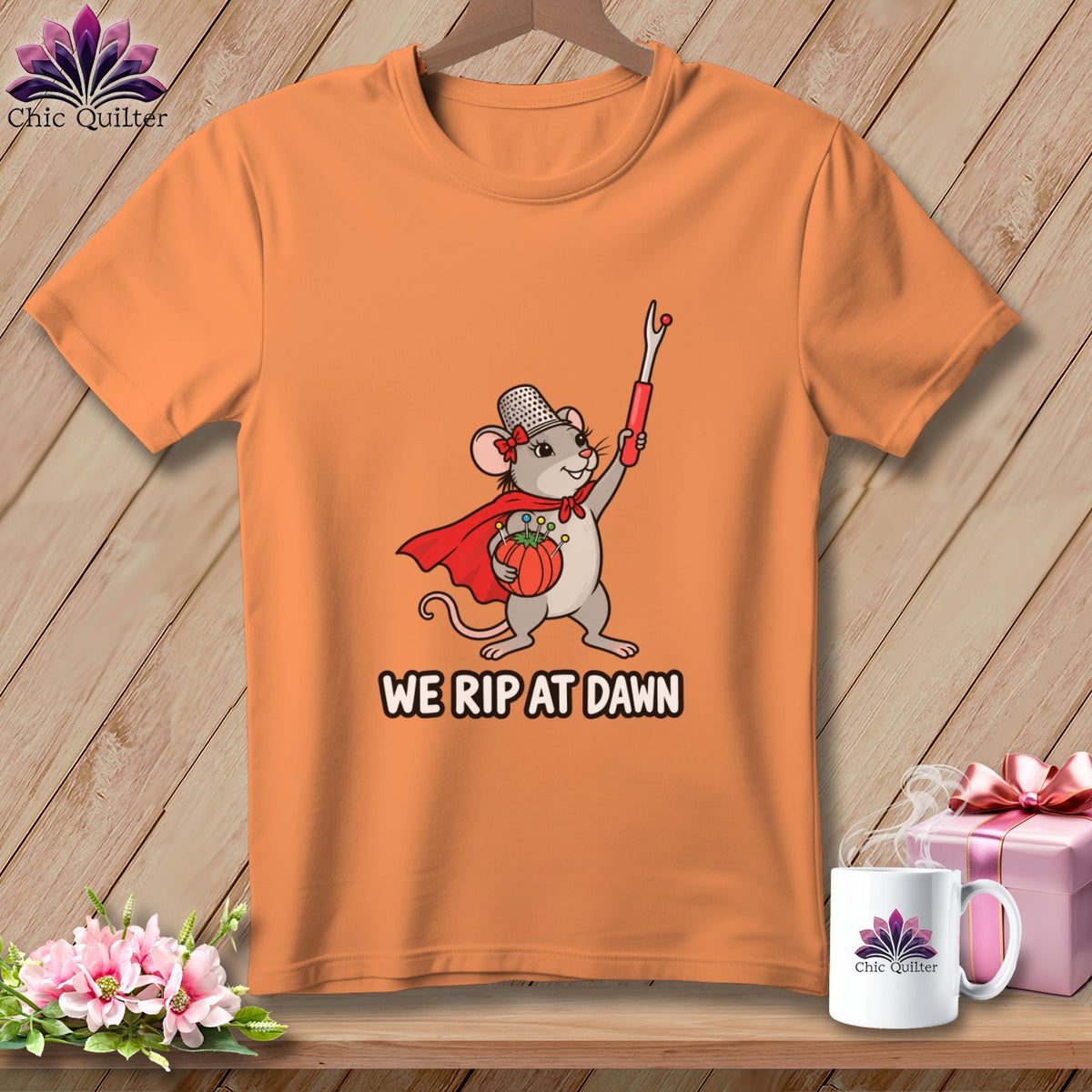 Orange crewneck t-shirt featuring a superhero mouse holding a seam ripper and text reading WE RIP AT DAWN.