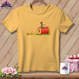 Yellow t-shirt featuring an illustration of a woman riding a large red spool of thread.