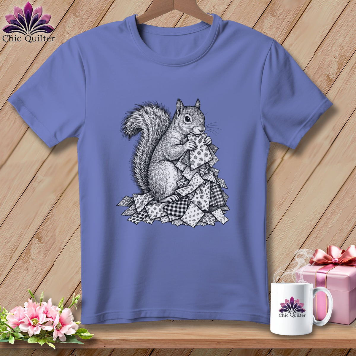 A periwinkle blue short-sleeve t-shirt featuring a black and white sketch of a squirrel holding patterned quilt scraps.