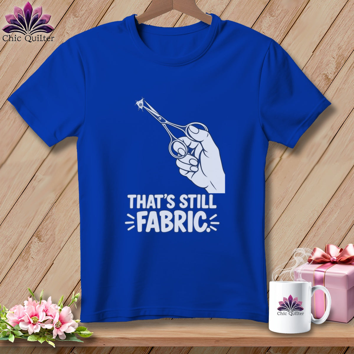 Blue t-shirt with graphic of hand holding scissors cutting fabric and text "THAT'S STILL FABRIC."