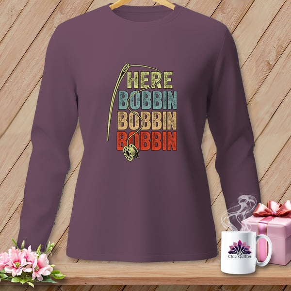 Long-sleeve purple shirt with vintage "HERE BOBBIN" text and sewing needle graphic.