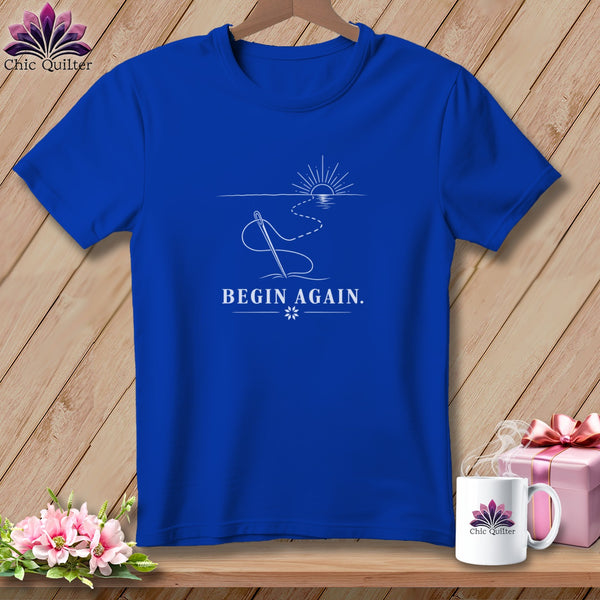 Blue t-shirt with "BEGIN AGAIN." text, needle, thread, and sun graphic.