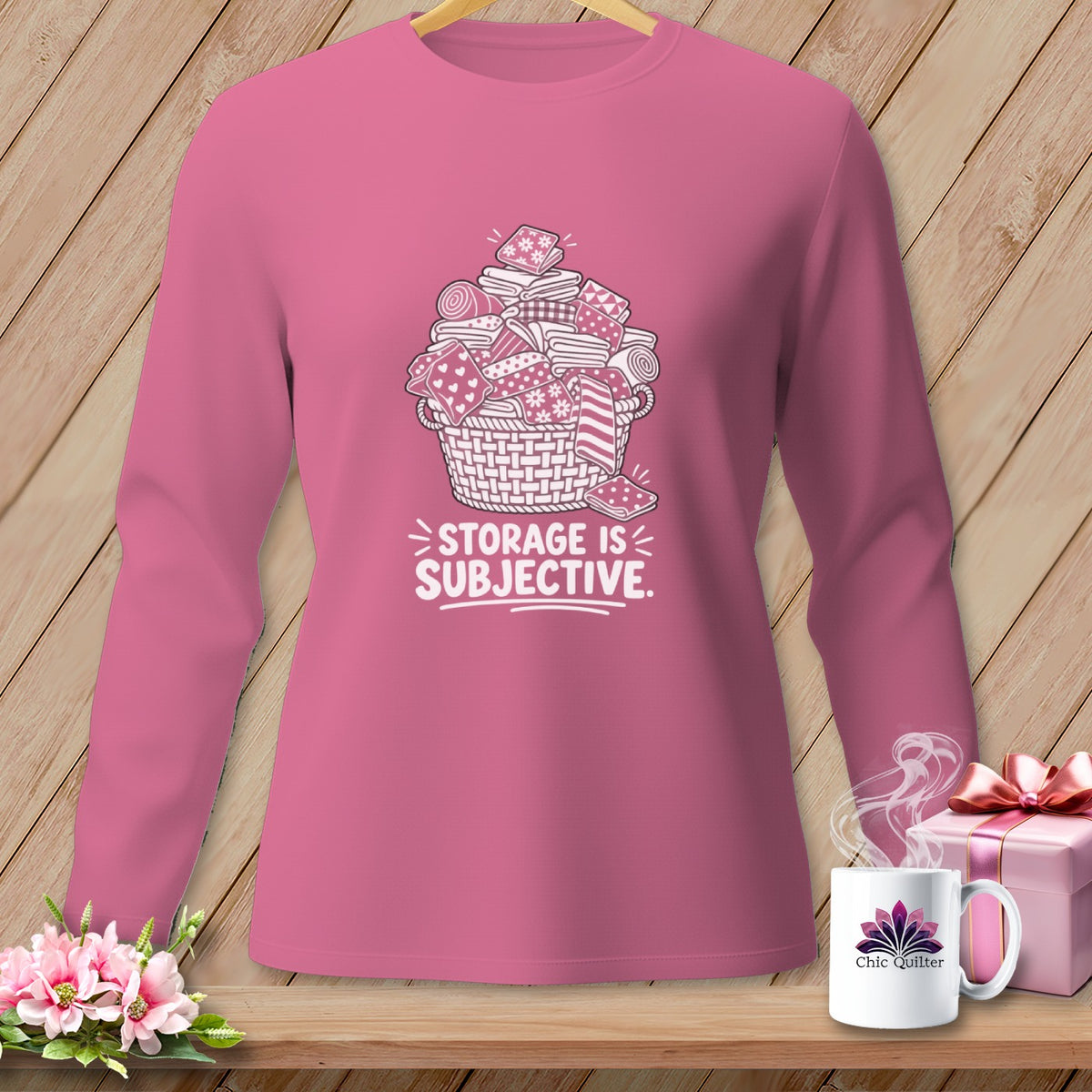 Pink long-sleeve shirt with graphic of a basket overflowing with fabric scraps and text "STORAGE IS SUBJECTIVE."