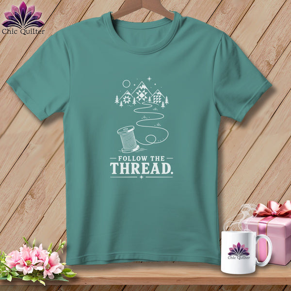 Teal t-shirt with "Follow the Thread" graphic of spool, mountains, and quilt blocks.