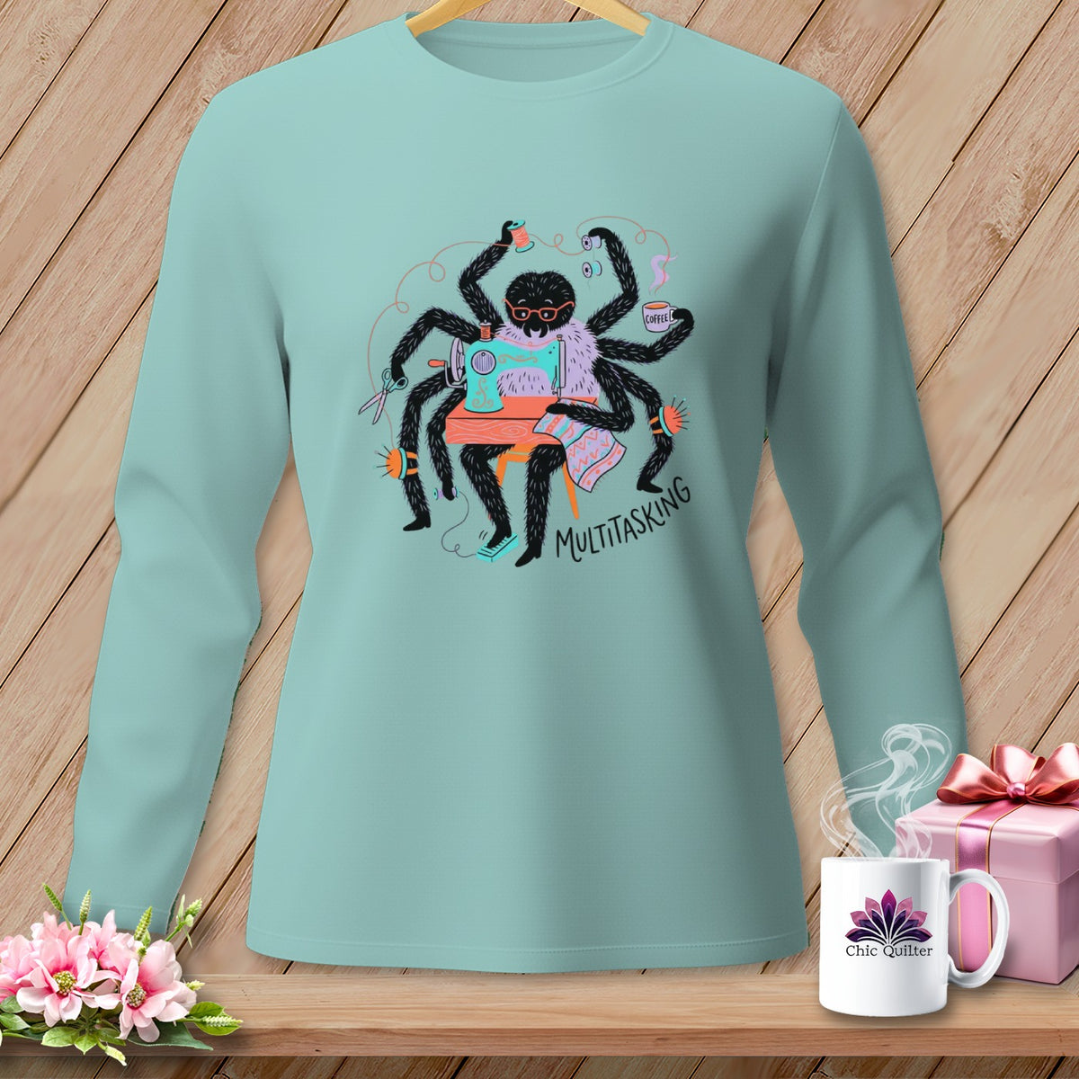 Spider sewing and drinking coffee with "MULTITASKING" text on a light blue long-sleeve shirt.