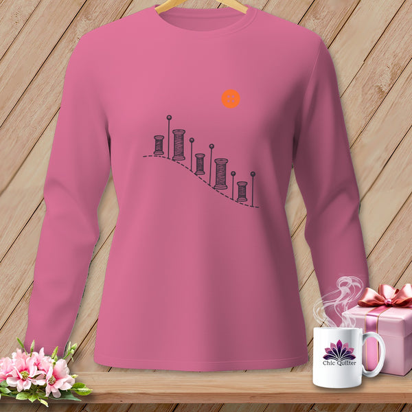 Pink long-sleeve shirt with sewing spool graphic and orange sun.