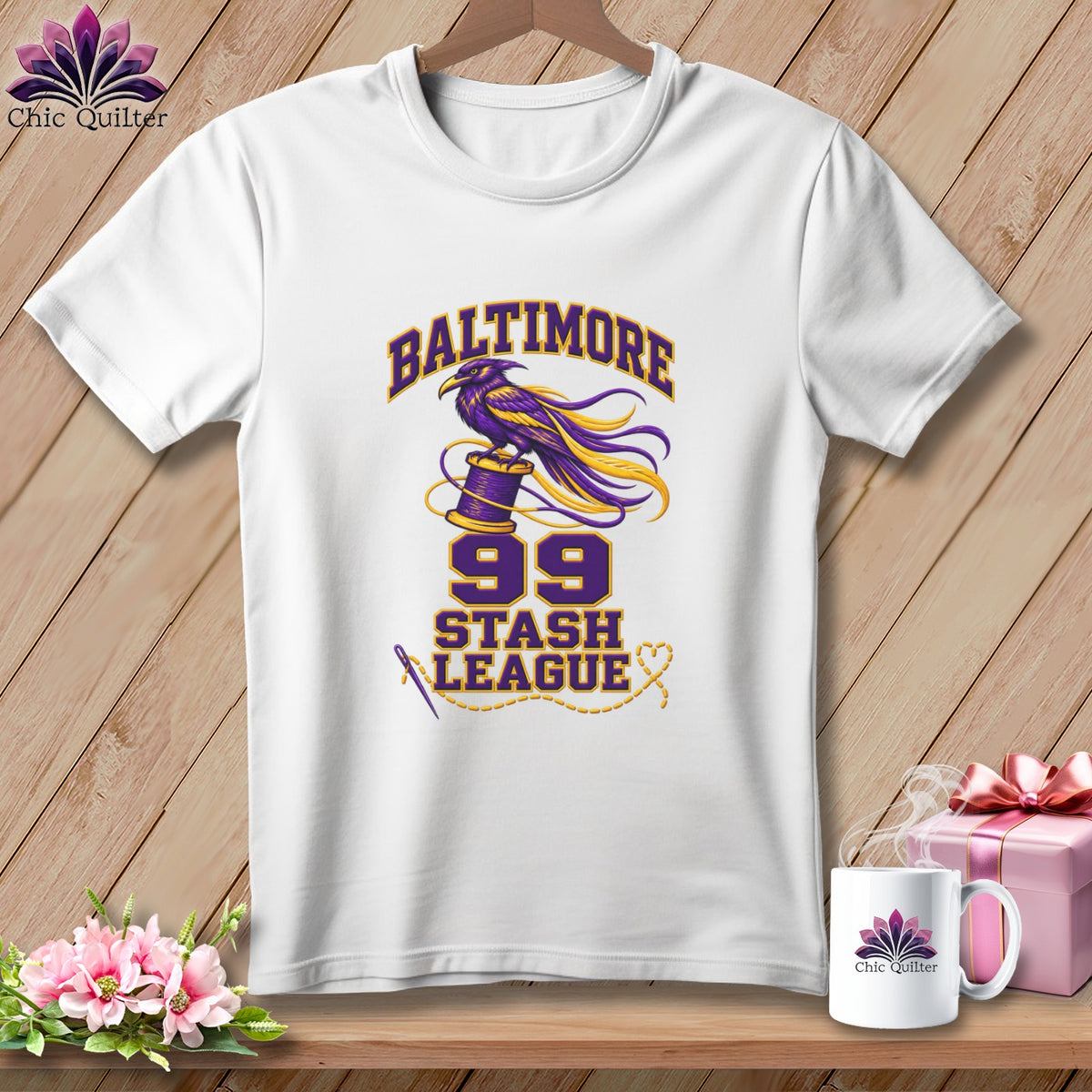 A white t-shirt features a graphic with a purple and gold raven on a spool, text reading Baltimore 99 Stash League, and a needle and thread.