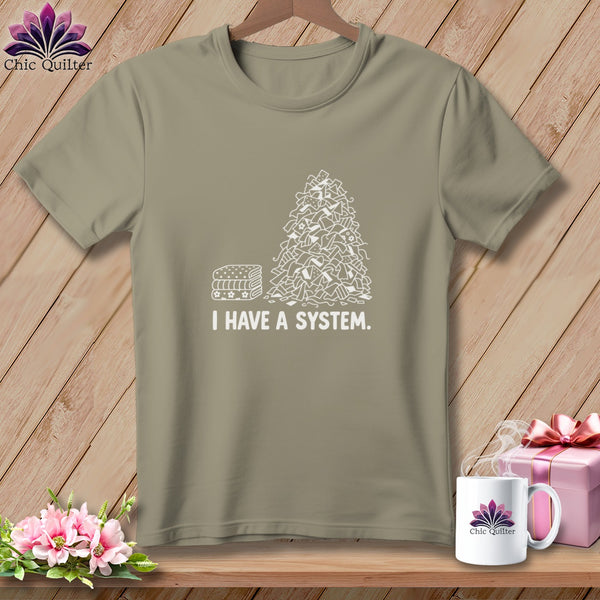 T-shirt with a pile of fabric scraps and stacked fabric labeled "I HAVE A SYSTEM."