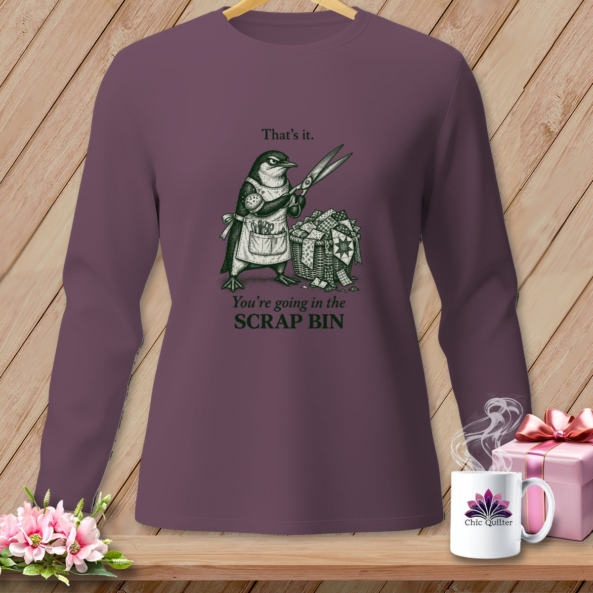 Penguin with scissors and fabric scraps on a purple long-sleeved shirt.