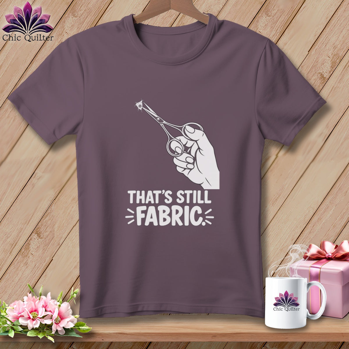 Purple t-shirt with graphic of hand holding scissors cutting fabric and text "That's Still Fabric".
