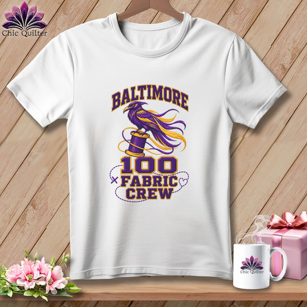 White t-shirt with a purple and yellow graphic featuring a raven, a spool of thread, and Baltimore 100 Fabric Crew text.
