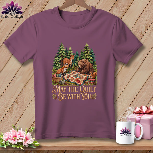 A mauve t-shirt featuring a forest graphic with woodland animals and the text "May the Quilt Be With You."