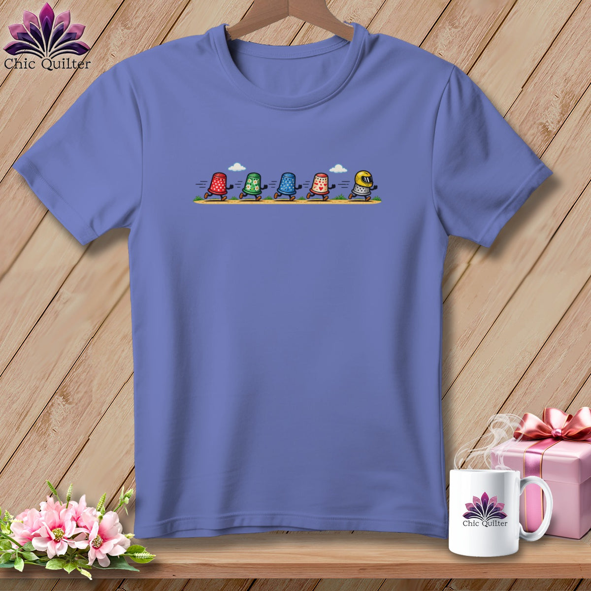 Periwinkle t-shirt featuring a cartoon graphic of five thimbles running across a path.