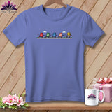 Periwinkle t-shirt featuring a cartoon graphic of five thimbles running across a path.