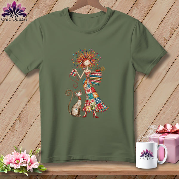 An olive green t-shirt displays an illustration of a woman in a patchwork dress with a cat.