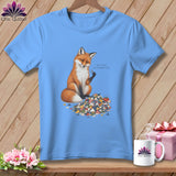 Light blue t-shirt with a fox sitting on a pile of fabric scraps, holding a needle and thread.