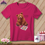 Pink t-shirt with a sad bear, quilt block, and spool of thread.