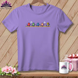 Light purple t-shirt featuring a graphic of five animated thimbles racing, displayed on a wooden background.
