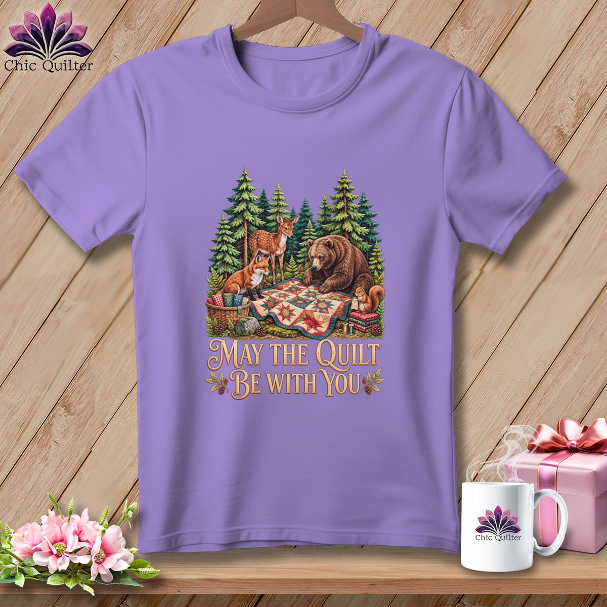 A light purple t-shirt featuring a forest scene with woodland animals and the text May the Quilt Be With You.