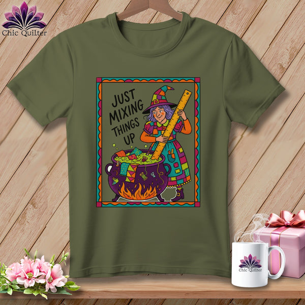 Green t-shirt with a cartoon witch stirring a cauldron with a ruler, text "JUST MIXING THINGS UP".