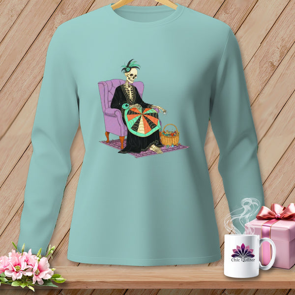 Skeleton sitting in a chair, sewing a colorful quilt, with a mug that says "Chic Quilter."