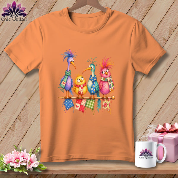 Orange t-shirt featuring an illustration of four colorful cartoon birds wearing scarves on a knitting needle.