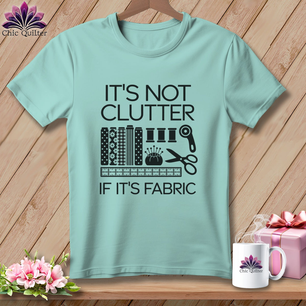 Light blue t-shirt with black text and sewing graphics: "IT'S NOT CLUTTER IF IT'S FABRIC".