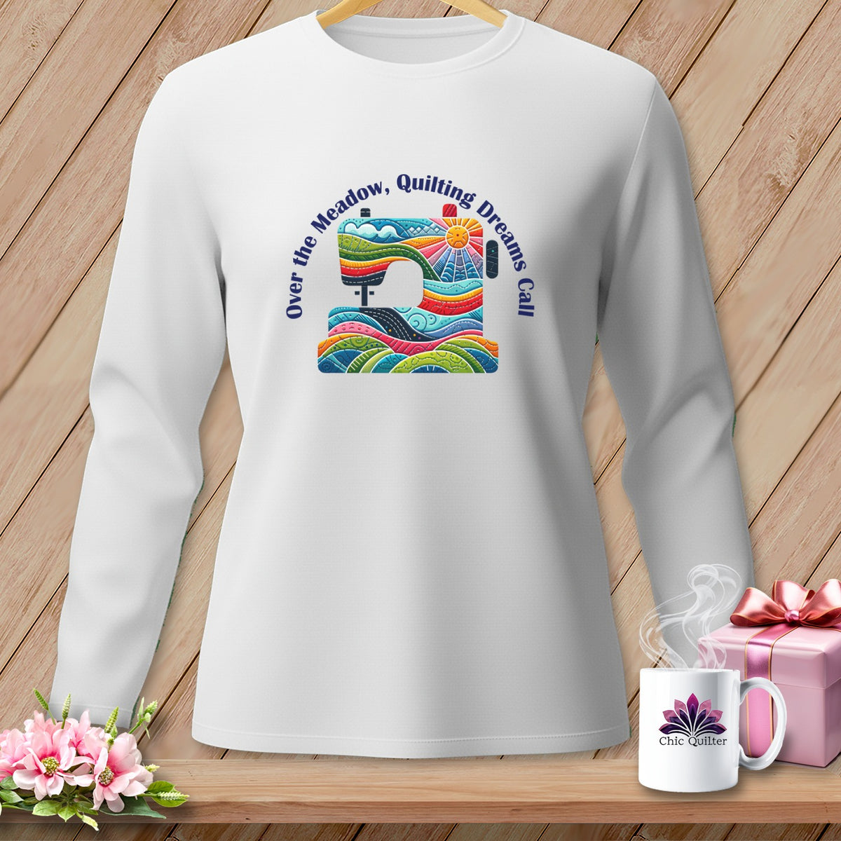 White long-sleeve shirt with colorful sewing machine graphic and "Over the Meadow, Quilting Dreams Call" text.