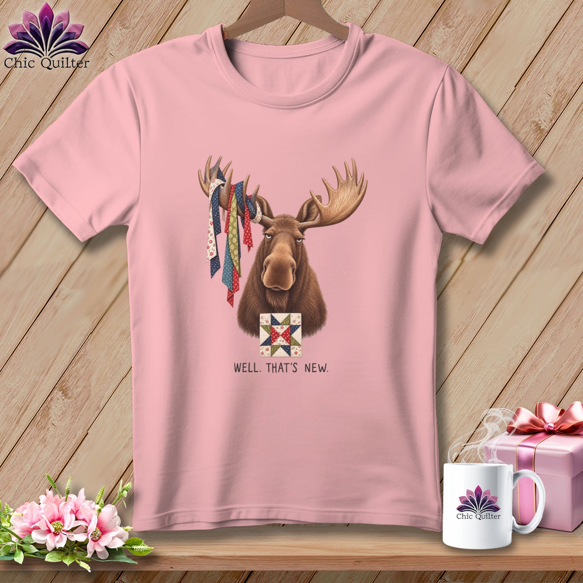 Pink t-shirt with a moose holding quilt scraps and a quilt square, text reads WELL. THAT'S NEW.