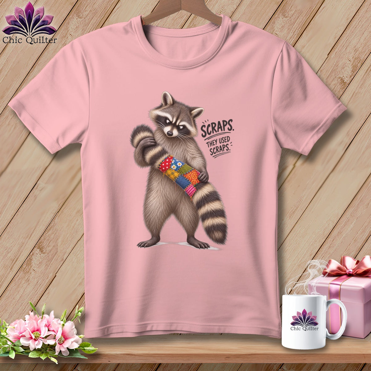 Pink t-shirt with raccoon holding quilt scraps and text "Scraps. They used scraps."