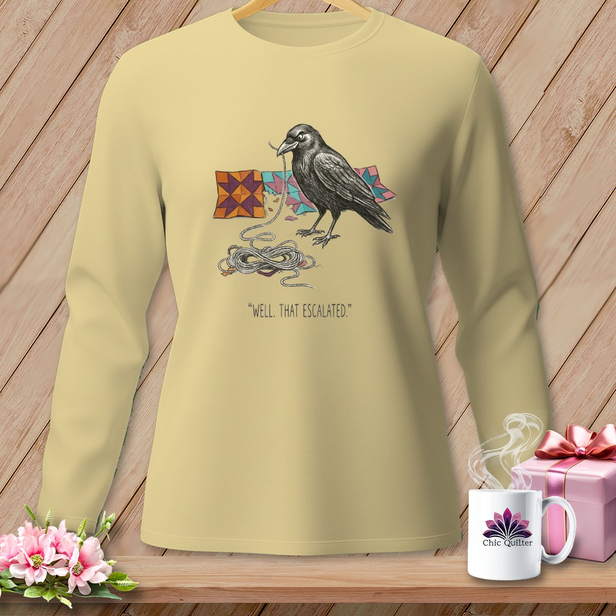 Crow with yarn and quilt squares graphic on a light yellow long-sleeve shirt.