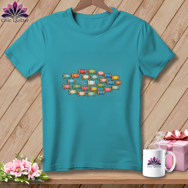 Turquoise t-shirt featuring a graphic print of colorful spools of thread arranged on a wooden background.