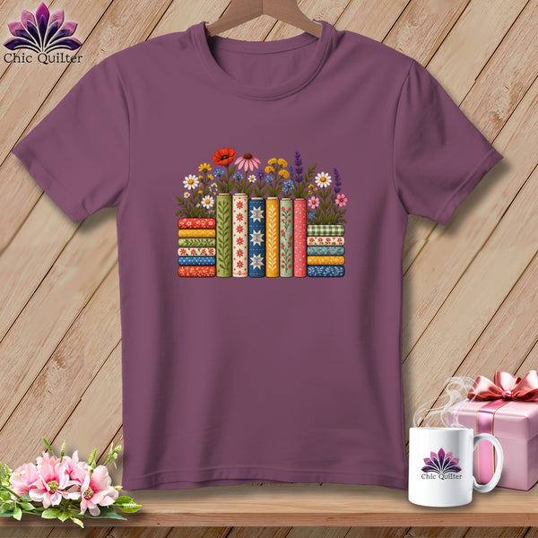 Maroon crewneck t-shirt featuring a graphic of books with colorful floral patterns and stems on a wooden background.