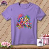 A purple crewneck t-shirt featuring two colorful cartoon owls on a branch with sewing accessories.