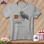 Grey t-shirt with a drawing of a crow holding thread and colorful quilt blocks, with text.
