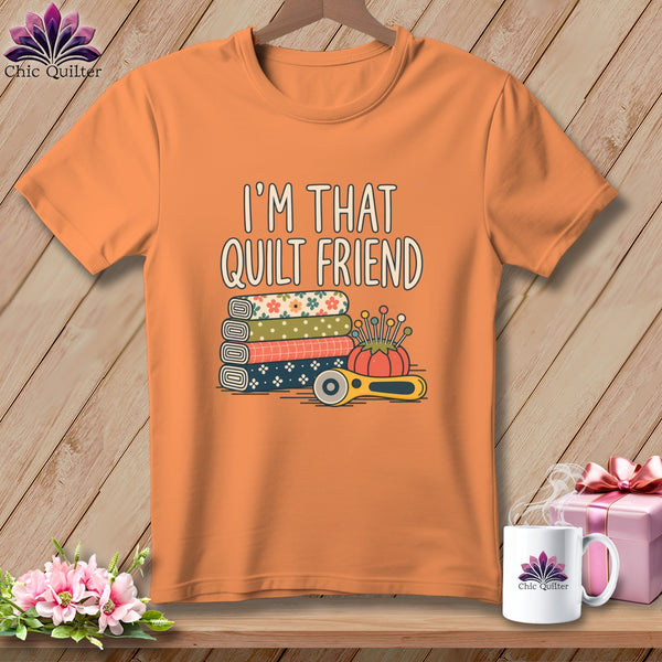 An orange t-shirt printed with the text I'm That Quilt Friend, stacked fabrics, pins, and a rotary cutter.