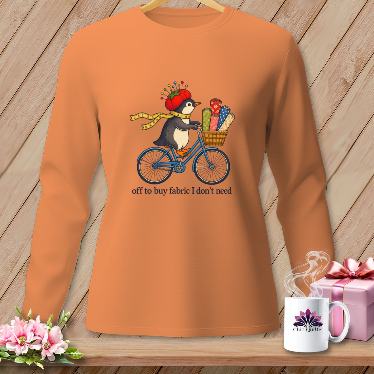 Orange long-sleeve shirt with a penguin on a bicycle, carrying fabric.