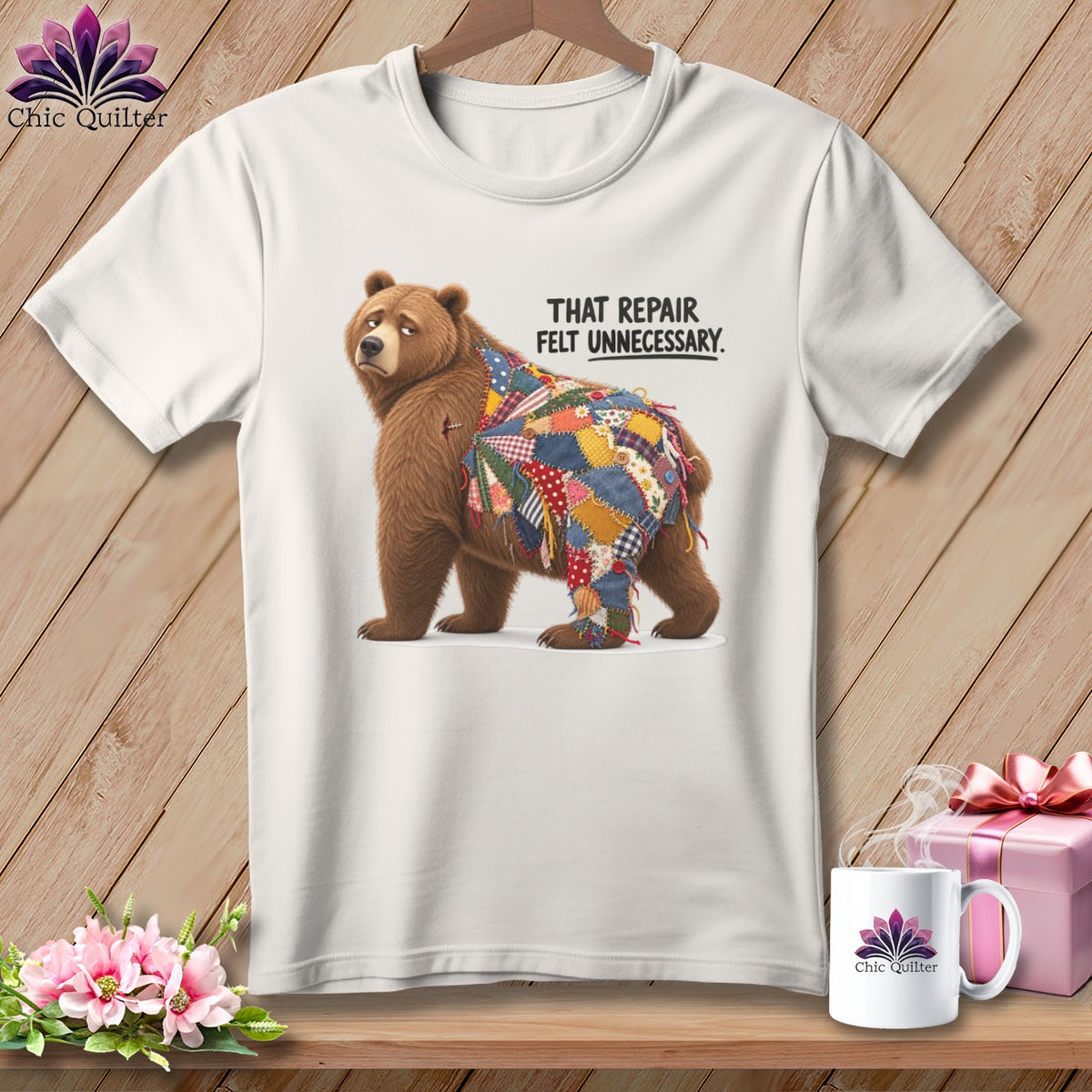 White t-shirt with a bear wearing a patchwork blanket, reading "That repair felt unnecessary."