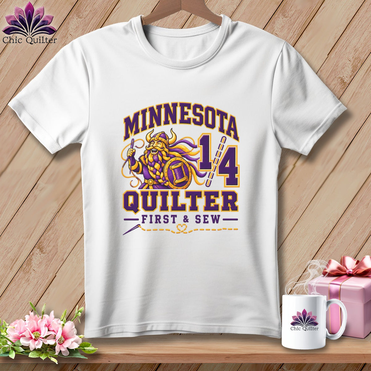 A white t-shirt hanging against a wooden background, featuring purple and yellow text reading Minnesota Quilter First and Sew.