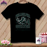 A black t-shirt featuring a green and white graphic with an eagle holding a needle, text reading Philadelphia Quilter 1/4, and a sewing theme.