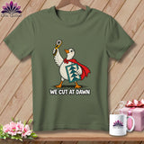 An olive green t-shirt features a graphic of a superhero duck holding a rotary cutter and quilt block, with the text WE CUT AT DAWN.