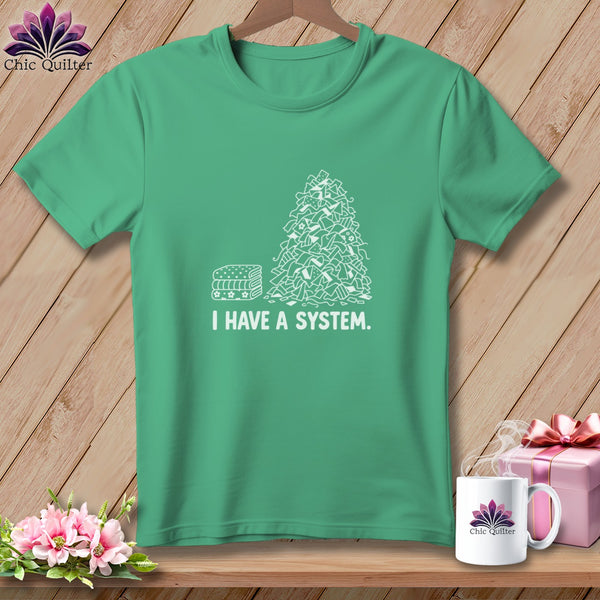 Green t-shirt with white graphic of stacked fabric and pile of fabric scraps with text "I HAVE A SYSTEM."