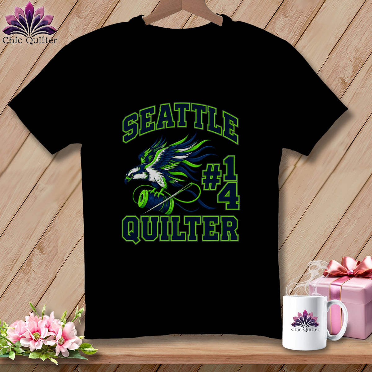 A black t-shirt features a green and blue graphic of an eagle, a spool of thread, and the text Seattle Quilter #14.